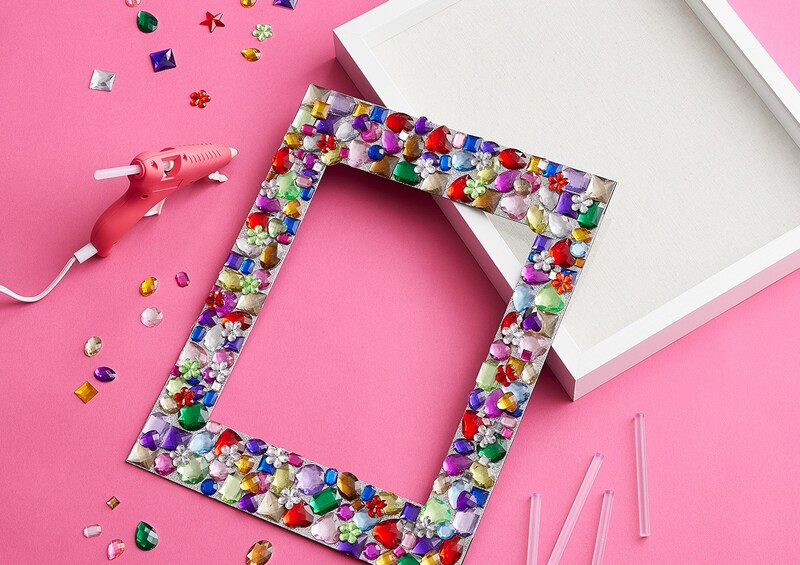 Bejeweled frame with jewels and glue gun on a pink table
